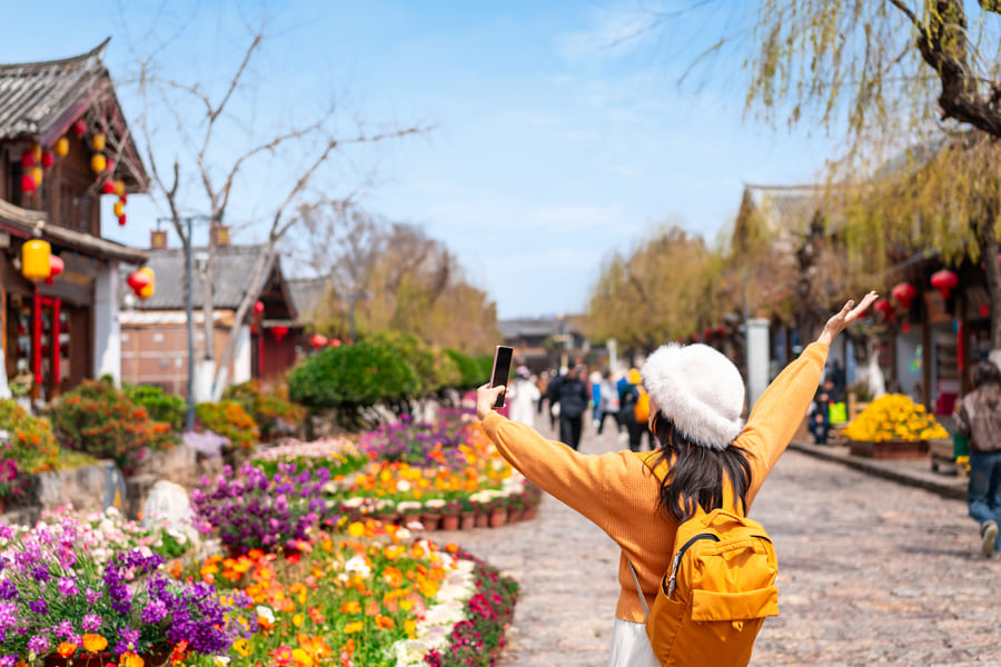 Viajera hispanohablante con mochila explorando las calles tradicionales de Lijiang, China, durante un viaje personalizado de turismo cultural.